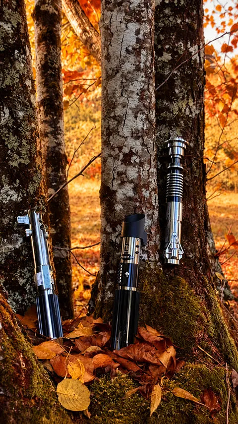 Trois poignées de sabres laser argentées et noires au pied d’un arbre
