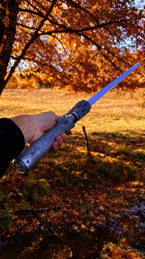 Sabre laser à lame bleue tenu en main sous les arbres