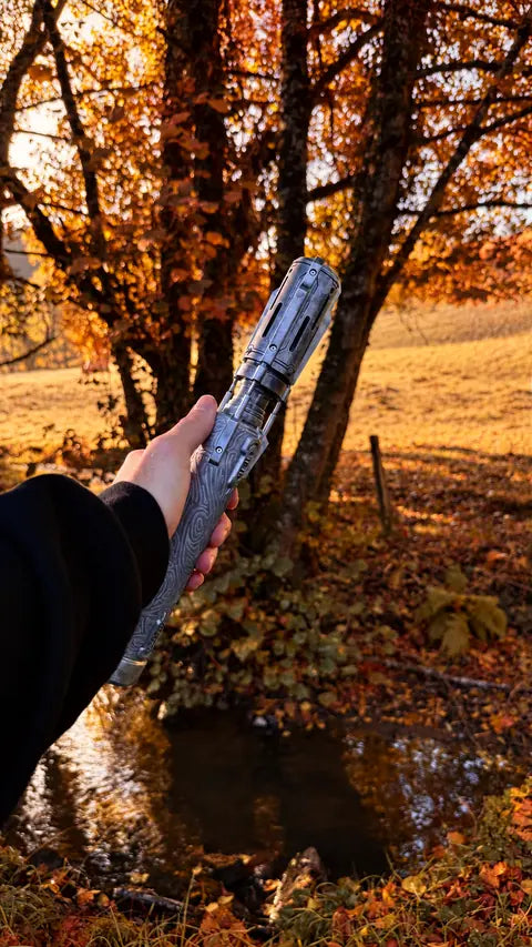 Poignée de sabre laser argentée et gravée présentée en main