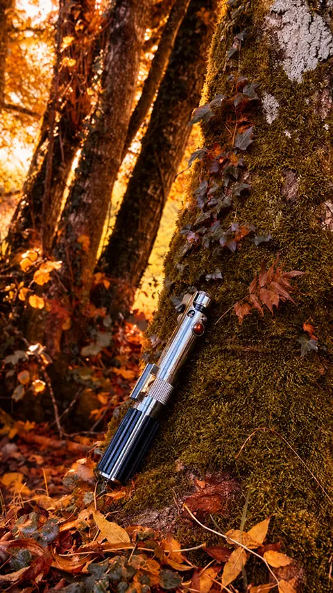 Poignée de sabre laser argentée posée contre un arbre en automne