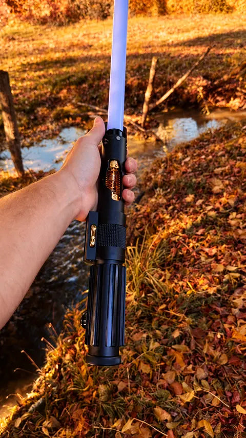 Sabre laser à lame claire présenté en main dans la forêt