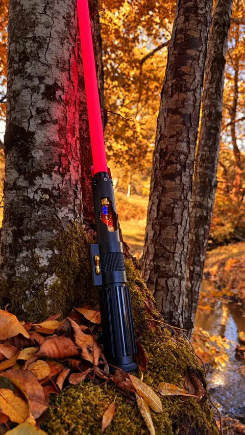 Sabre laser à lame rouge posé au pied des arbres