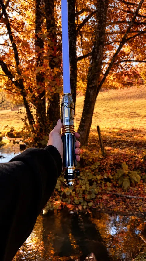 Poignée de sabre laser à col fin présentée en main dans un sous-bois