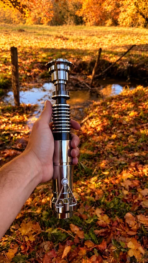 Poignée de sabre laser chromée à anneaux présentée en main au bord du ruisseau