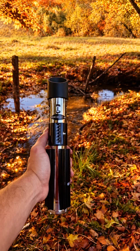 Poignée de sabre laser noire et chromée présentée en main près du ruisseau