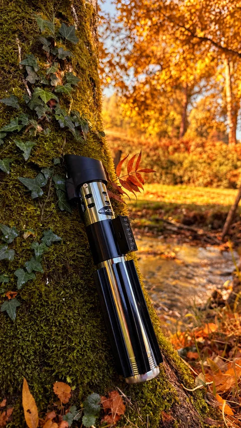 Poignée de sabre laser noire et chromée contre un arbre au bord de l’eau